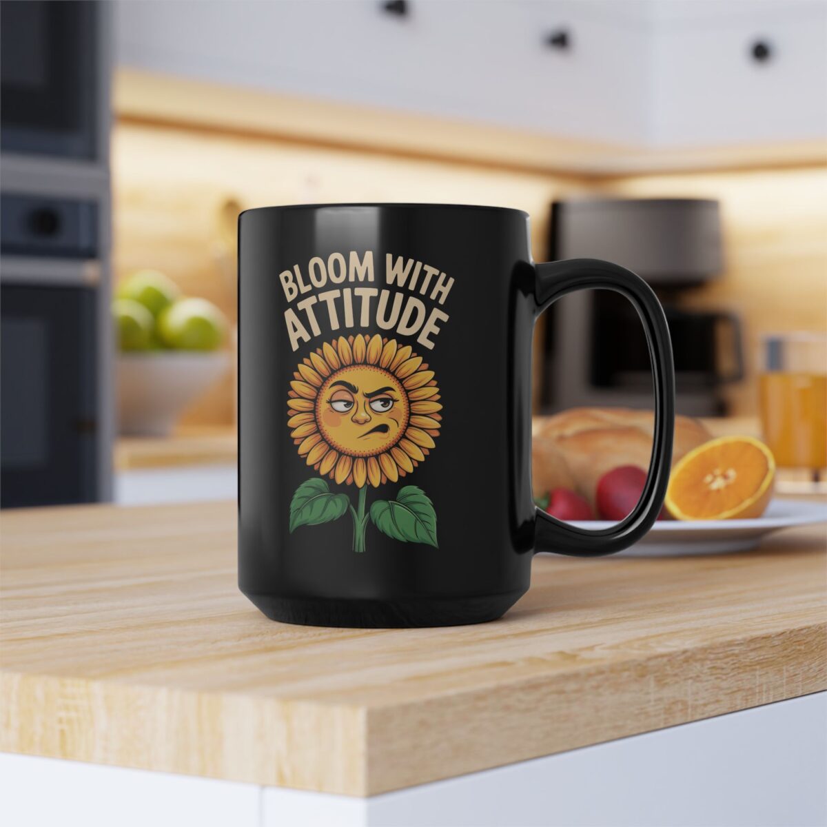 A black mug with a cartoon sunflower that has a grumpy face and reads "BLOOM WITH ATTITUDE". The mug is on a wooden countertop with a blurred kitchen background.