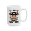 A white ceramic mug with a grumpy cartoon cow and flowers, saying 