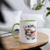 White ceramic mug with a green handle and rim, featuring a cute sloth in a hammock with the text 