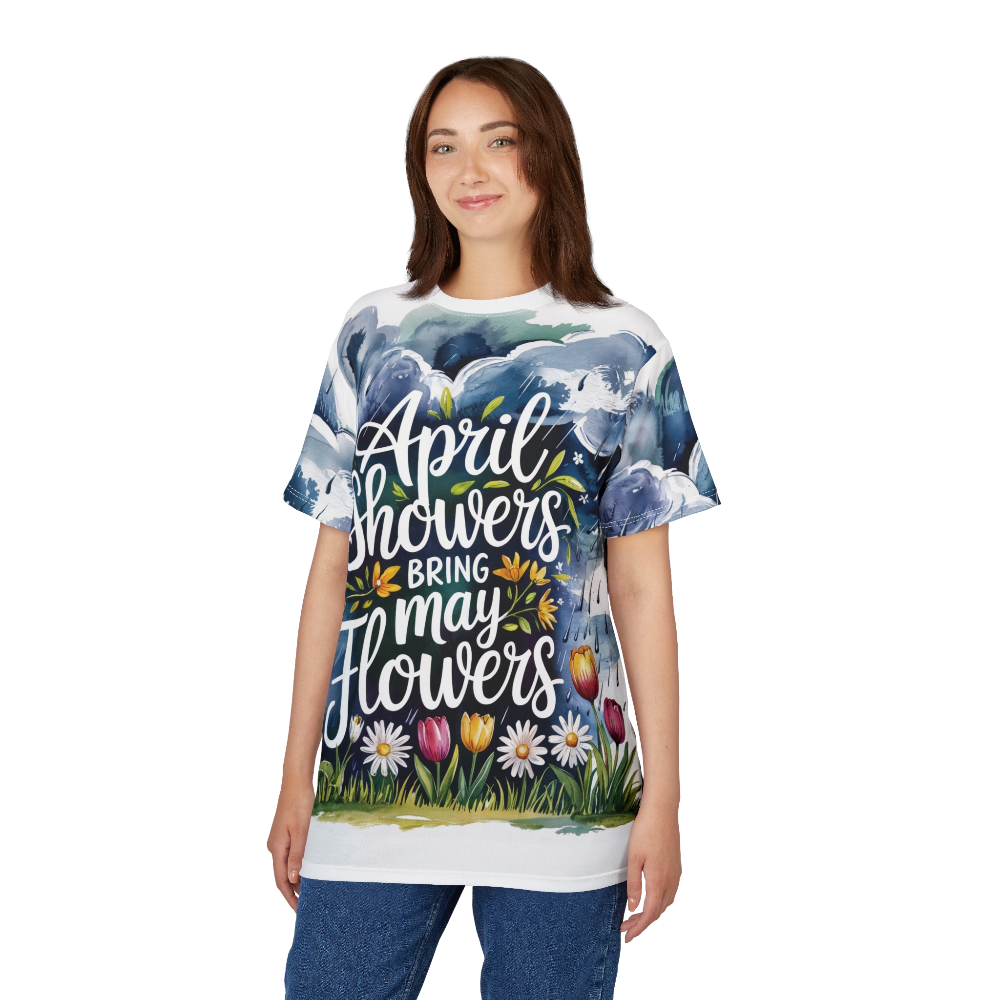Blue and green watercolor clouds with rain streaks and a field of colorful tulips and daisies cover this patterned tee shirt, with white script reading "April showers bring May flowers".