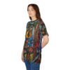A woman wearing a t-shirt with a vibrant, abstract painting of a cat's face. The design features bold colors like blue, yellow, orange, and brown, with swirling patterns and stylized floral elements. The t-shirt has a crew neck and short sleeves and is worn by a woman with long brown hair, standing with her hands behind her back.