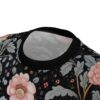 Black background with large pink flowers, detailed grey leaves, and small red and yellow blooms cover this patterned tee shirt.