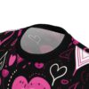 A close-up view of the collar and upper chest area of a black t-shirt with a repeating pattern of pink and white hearts and abstract shapes.