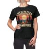 Black graphic t-shirt with retro sunset, campfire, tent, and trees design. Text reads 'LIFE IS BETTER AROUND THE CAMPFIRE'.