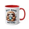 Cute sloth holding a blue polka dot mug and the text 'Busy Doing Nothing' on a white mug with red handle and interior.