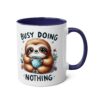 White ceramic mug with navy blue interior and handle. Features a cute sloth holding a polka-dot mug, surrounded by flowers and text.