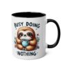 White ceramic mug with black interior and handle, featuring a cute sloth holding a polka dot cup and the text "BUSY DOING NOTHING".