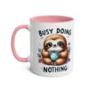 White ceramic mug with pink handle and interior, featuring a cartoon sloth holding a polka-dot mug and the words "BUSY DOING NOTHING".