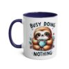 White ceramic mug with a navy blue interior and handle, featuring a cartoon sloth holding a polka-dot cup.