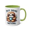 White ceramic mug with a green handle and interior, featuring a cute sloth illustration and the text "BUSY DOING NOTHING."