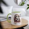 A white mug with a green handle and rim, showcasing a cute sloth holding a coffee cup.