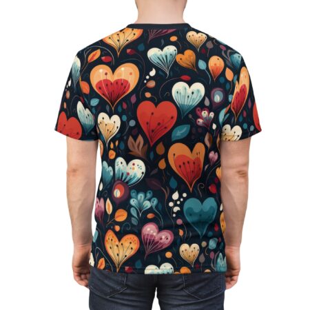 Back view of a person wearing a dark t-shirt with a repeating pattern of stylized heart-shaped flowers in vibrant colors like red, orange, yellow, and blue, accented with green leaves and small floral elements.