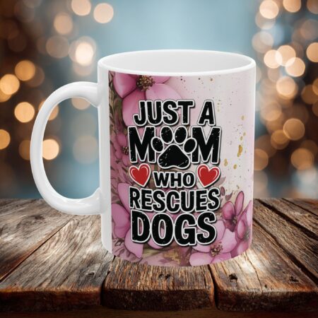 White ceramic mug with pink floral accents, featuring bold text 'JUST A MOM WHO RESCUES DOGS' and paw print.