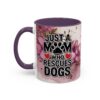 White ceramic mug with purple handle and interior, featuring a floral watercolor design and text "JUST A MOM WHO RESCUES DOGS" with paw print and hearts.
