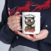 White ceramic mug with a cartoon cat wearing glasses and holding a pencil in its mouth.