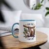 A white ceramic mug with a blue interior and handle, featuring a cartoon sloth hanging from a branch with leaves.