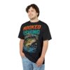 Orange and teal text, a jumping bass, and blue water splashes cover this 3D graphic t-shirt with a vibrant fishing theme.