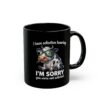 Black ceramic mug with a cartoon cow wearing glasses and eating grass, holding a text 