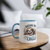 A white ceramic mug with a blue rim and handle, featuring a sleeping sloth graphic and the words "Natural Born Chiller".
