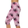 Close-up of a person wearing pink capri leggings adorned with a repeating black spider pattern, set against a white background.