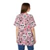Pink, black, and white floral and skull patterns cover this tee shirt, with detailed sugar skulls and blooming flowers.