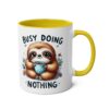 White ceramic mug with yellow interior and handle, featuring a cartoon sloth holding a polka dot cup with the text "BUSY DOING NOTHING".