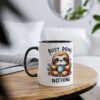 White ceramic mug with a black handle and rim, featuring a cute cartoon sloth holding a polka-dot mug with the text "BUSY DOING NOTHING."