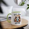 White ceramic mug with green handle and rim, featuring a cartoon sloth holding a polka dot cup and the text "BUSY DOING NOTHING".