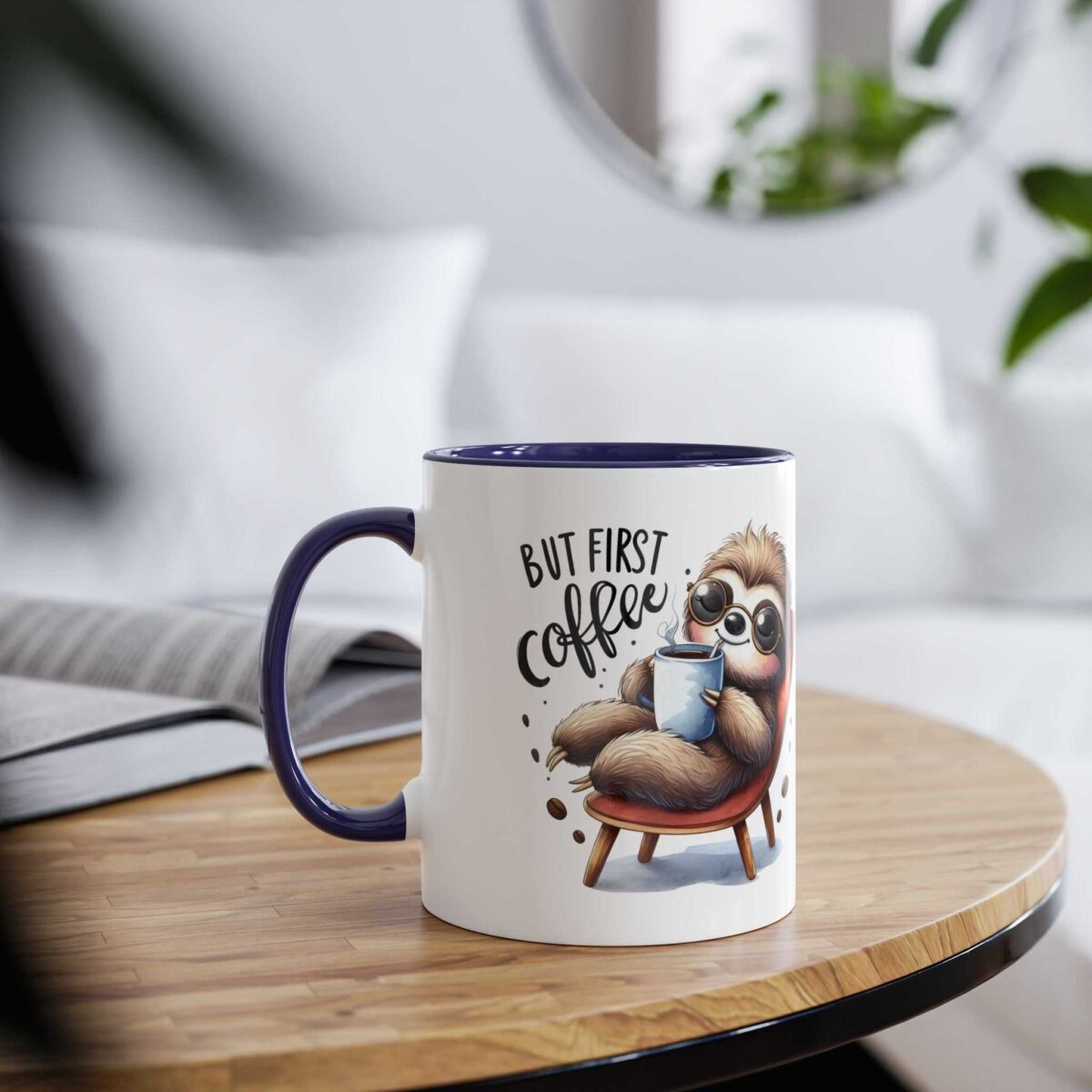 A white mug with a navy blue rim and handle, featuring a cartoon sloth holding a coffee cup and the words "BUT FIRST coffee".
