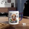 A white mug with a blue handle features a cute sloth holding a coffee cup, surrounded by leaves and coffee beans.