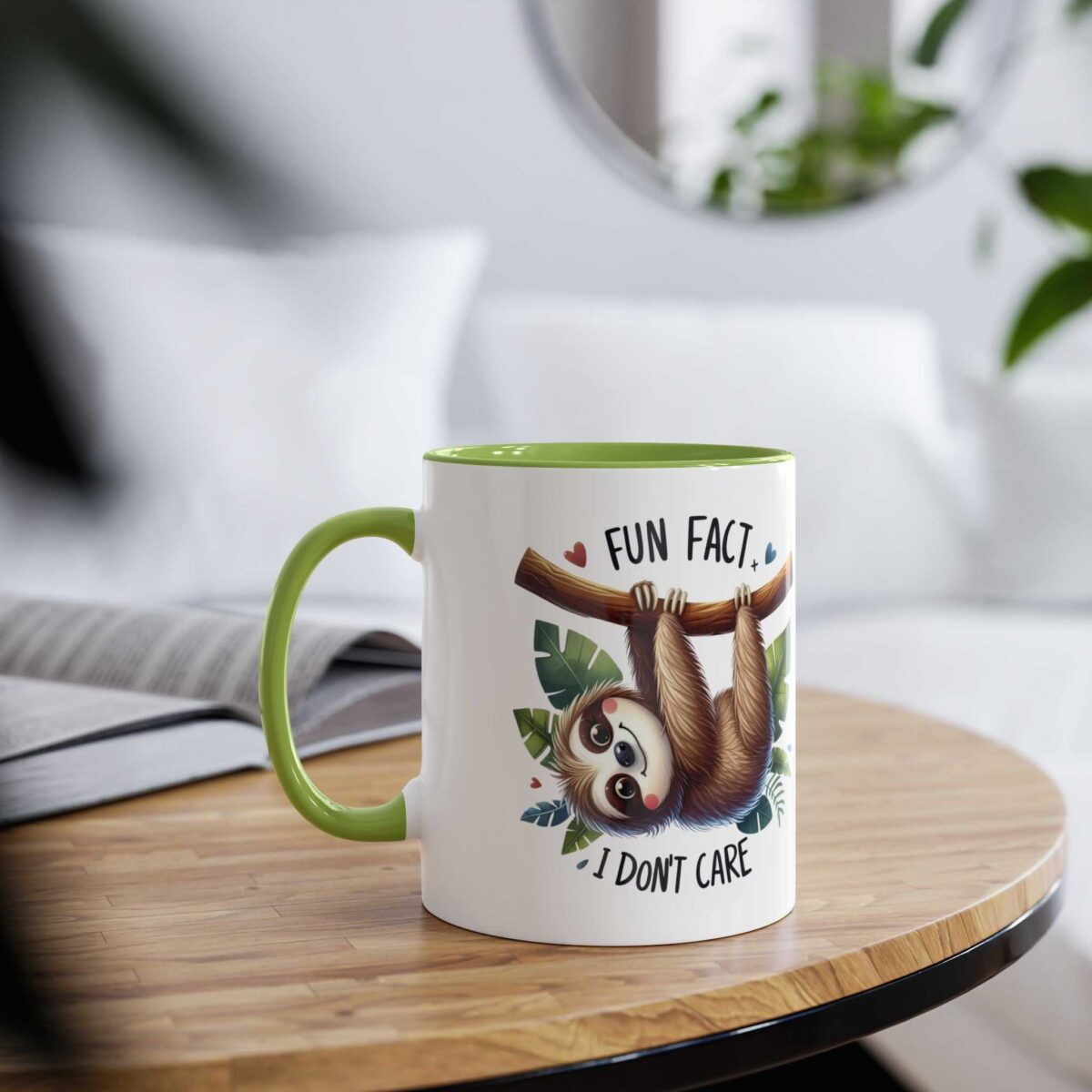 White ceramic mug with a green handle and rim, featuring a cartoon sloth hanging from a branch with text.