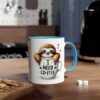 A white ceramic mug with a blue rim and handle, featuring a cartoon sloth peeking out of a coffee cup with the text "I NEED COFFEE".
