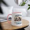 White ceramic mug with a pink handle and rim, featuring a sleeping sloth illustration and the text "NATURAL BORN CHILLER".