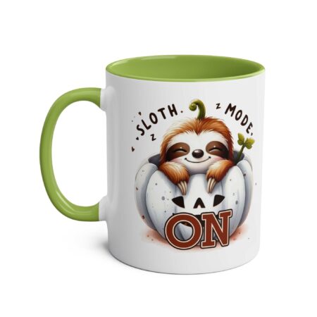 White ceramic mug with green handle and interior, featuring a smiling sloth peeking out of a white pumpkin.
