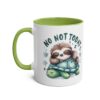 A white ceramic mug with a green handle and interior, featuring a cartoon sloth sleeping on a turtle.