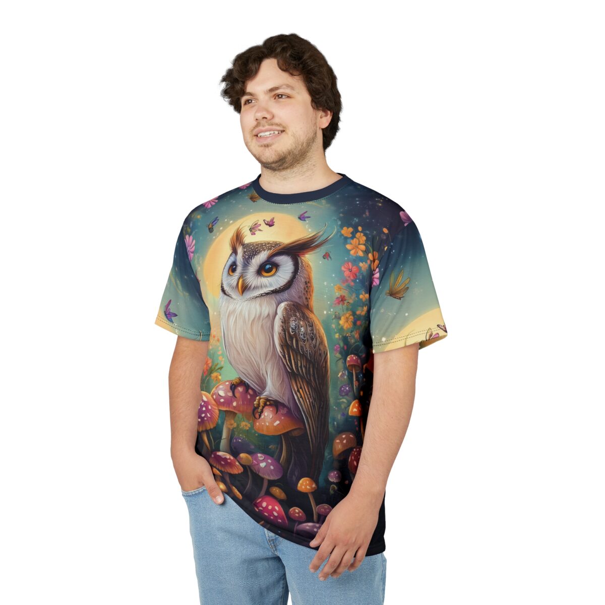 A man wearing a t-shirt with a fantasy design of an owl perched on mushrooms, surrounded by flowers and butterflies under a full moon.