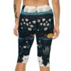 Capri leggings with a dark background featuring a pattern of white cats, yellow ducks, white daisies, and green reeds.