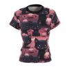 A women's t-shirt with a repeating pattern of cute black cats and smiling pumpkins, set against a pinkish-purple background with bats.