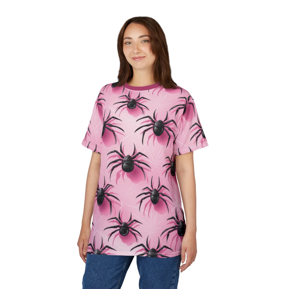 A smiling young woman models a vibrant pink t-shirt adorned with a repeating black spider pattern, paired with blue jeans.