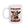 White ceramic mug with a cartoon cow holding a daisy and text that reads