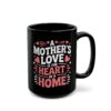 Black ceramic mug with white and pink text that reads 'A Mother's Love Is The Heart Of A Home', adorned with small hearts and stars.