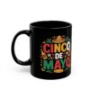 A black mug featuring a vibrant Cinco De Mayo design with a sombrero, maracas, and festive text surrounded by colorful splashes and a bottle.