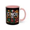 A vibrant Cinco De Mayo design featuring text, a Mexican flag, a sombrero, maracas, and festive patterns covers this black mug with a pink handle and interior.