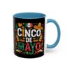 A black mug with a blue interior and handle features a vibrant 'Cinco De Mayo' design. Elements include a Mexican flag, sombrero, maracas, and festive patterns.