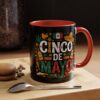 Black mug with a colorful Cinco De Mayo design featuring Mexican flag, sombrero, maracas, and festive text. The handle and interior are bright red.