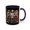 A black mug with a navy blue handle and interior features a vibrant Cinco De Mayo design with the Mexican flag, sombrero, maracas, bottles, and decorative elements.