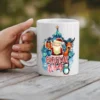 White ceramic coffee mug with a festive Christmas design featuring Santa, a reindeer, a penguin, a Christmas tree, and gifts.