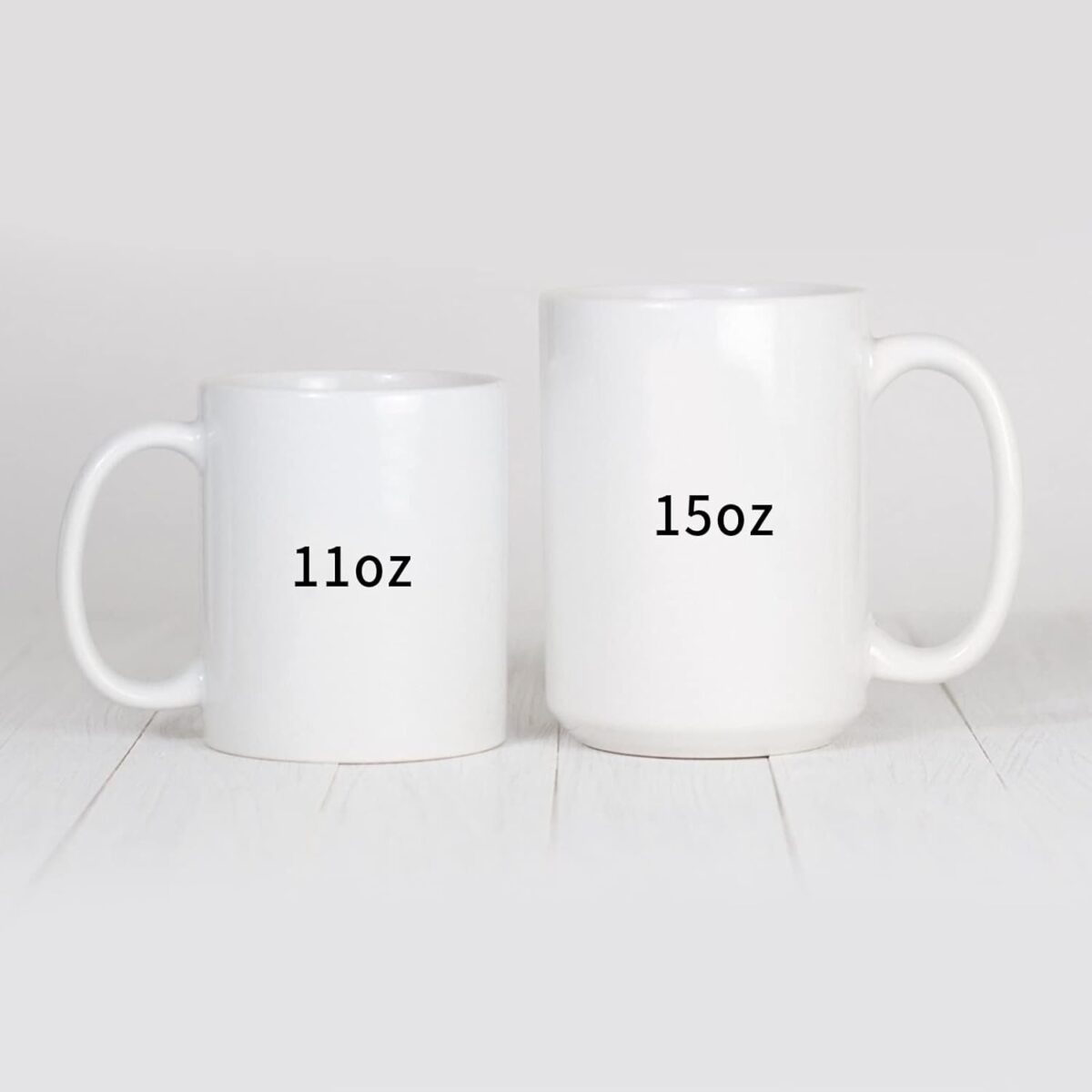 White ceramic coffee mugs displayed in 11oz and 15oz capacity sizes on a light wooden surface.