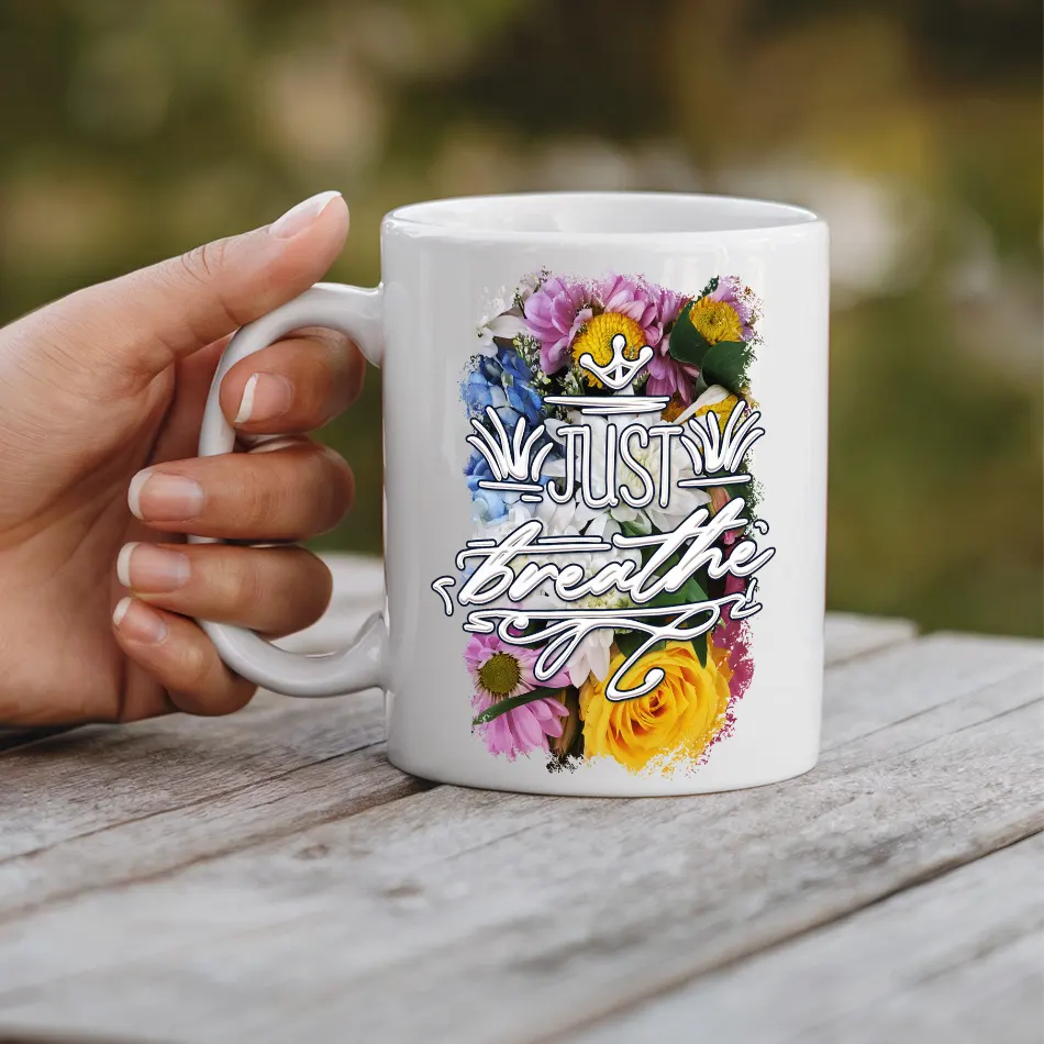White ceramic mug with colorful floral design and "Just Breathe" text.