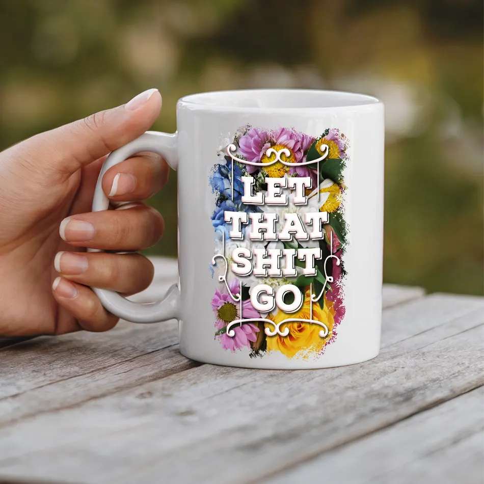 White ceramic mug with colorful floral design and bold text that reads "LET THAT SHIT GO".
